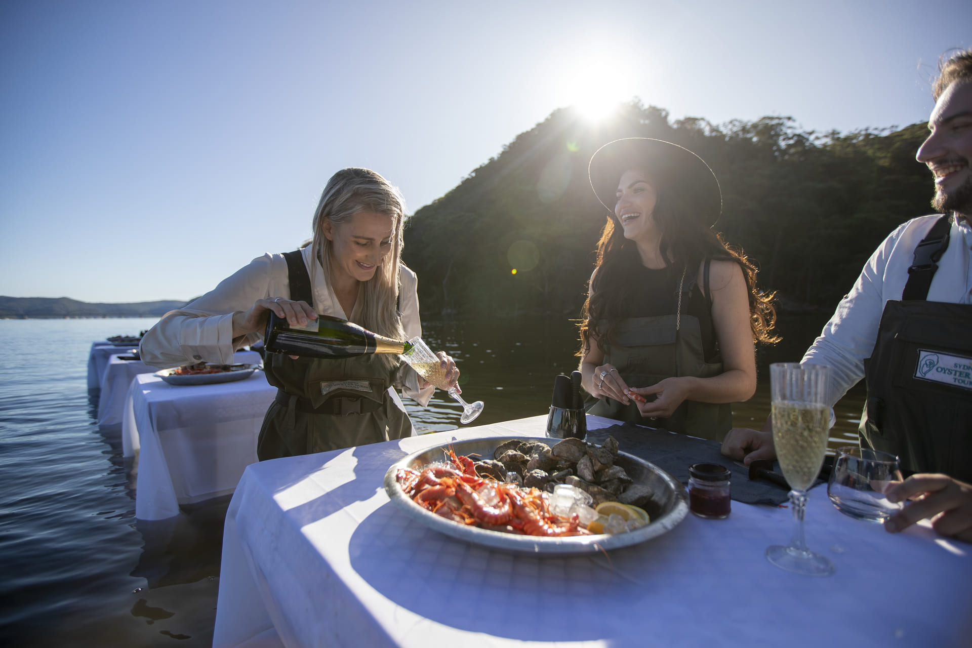 Guests in waders at an in-water table with oysters, prawns, and champagne on the Hawkesbury River